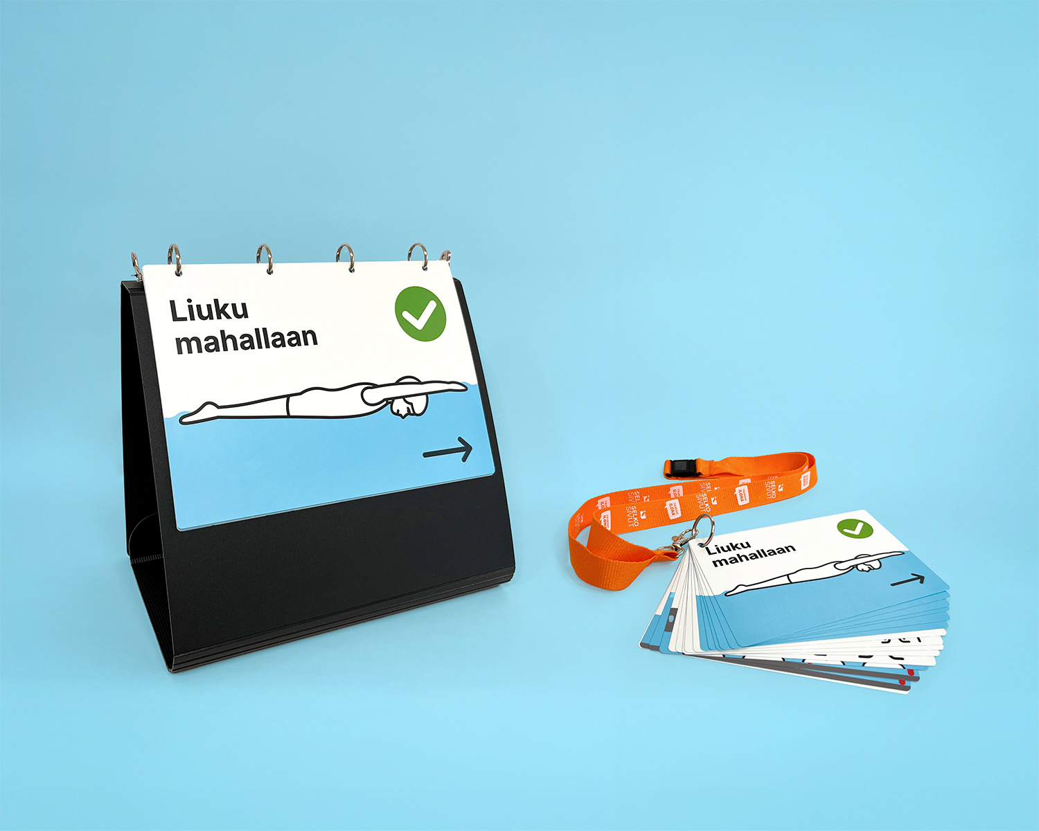 Kuvassa on pystyyn taitettu kuvakansio ja sen vieressä pienempiä kuvia kaulanauhassa.